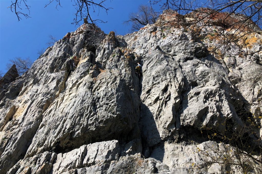 Two rock climbers scale a steep limestone cliff under a clear blue sky
