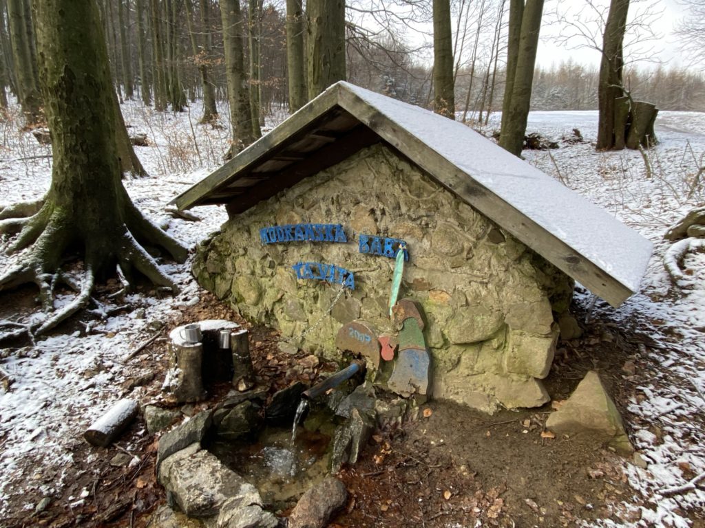 Water flows from a stone spring structure in a snowy forest