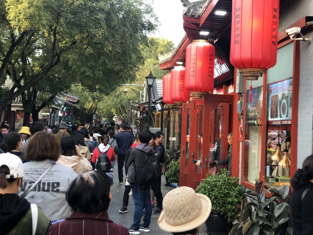 Crowd of people walking past a restaurant decorated with red lanterns in Beijing