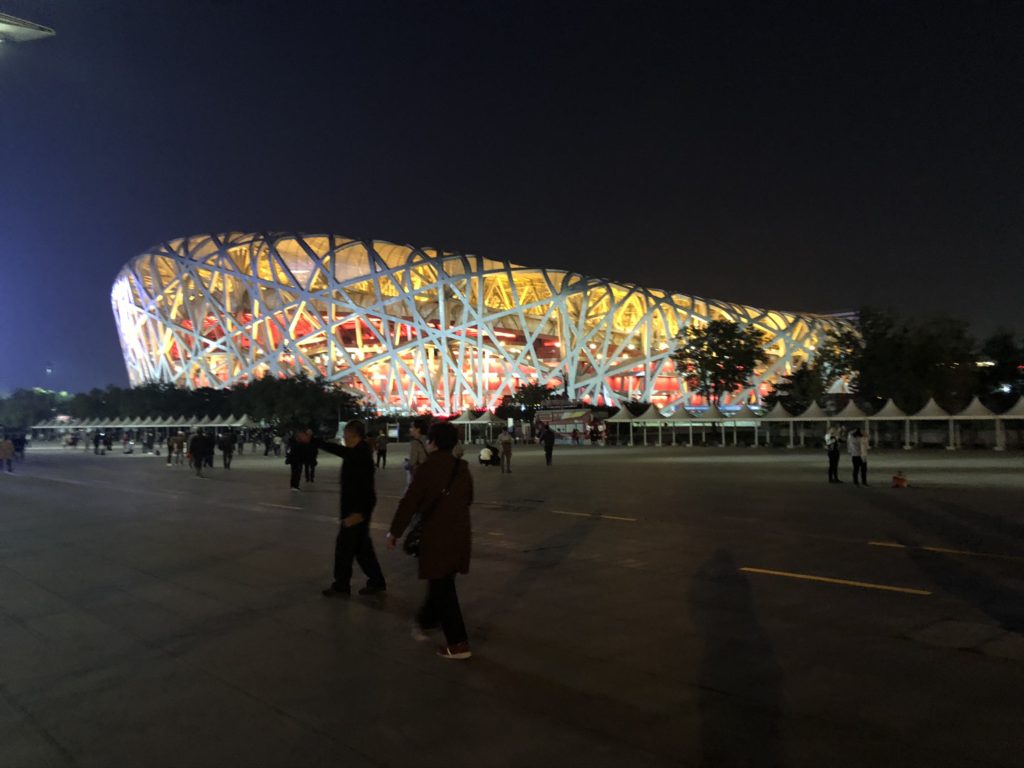 The Beijing National Stadium illuminated at night with people walking in the foreground