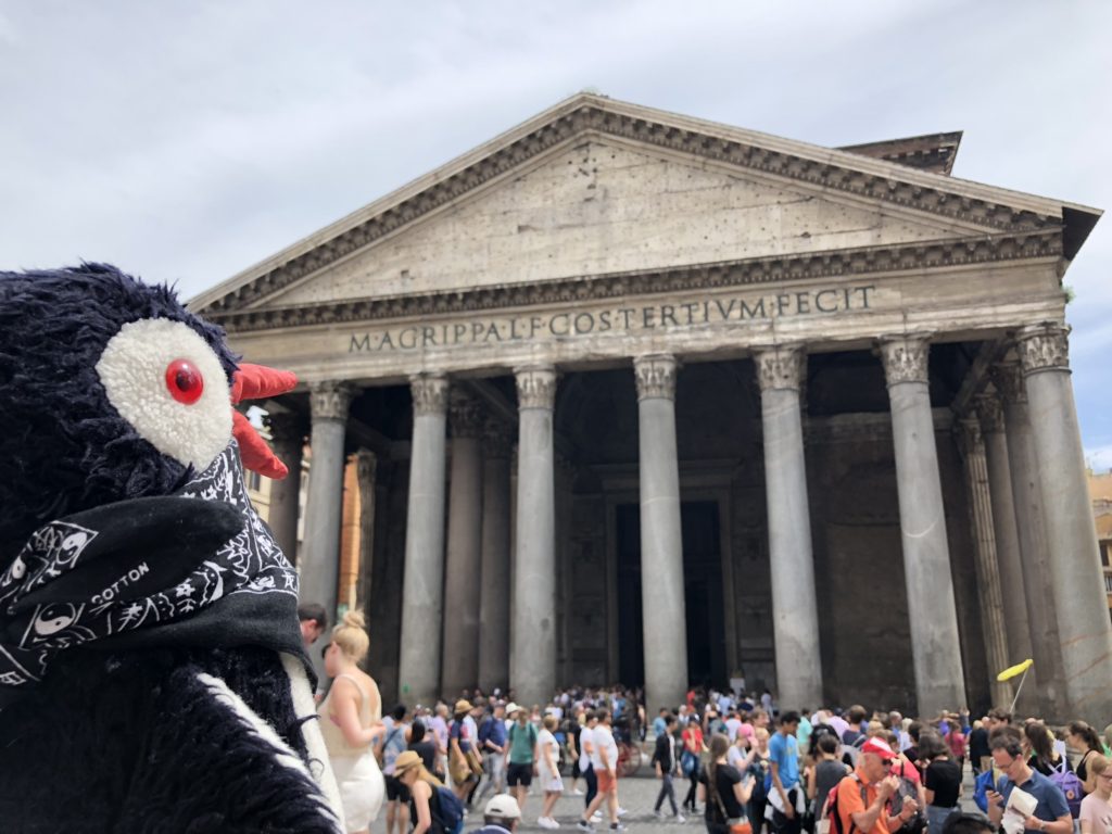Plush penguin Miško wearing a black bandana in front of the Pantheon in Rome