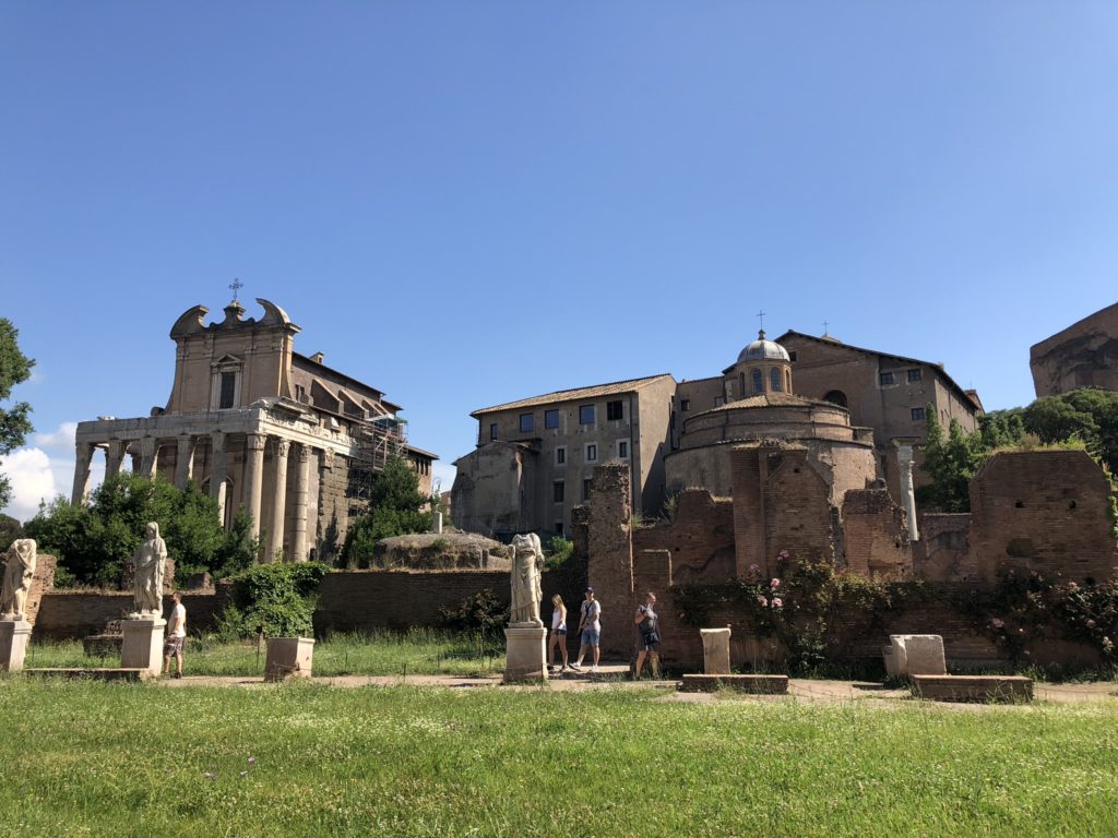 Tourists walk past ancient ruins and historic buildings in Rome, Italy