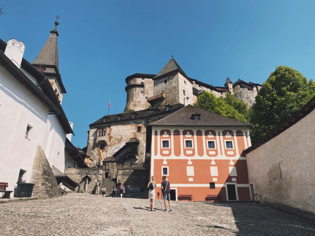 Tourists standing in the cobblestone courtyard of Orava Castle under a clear blue sky