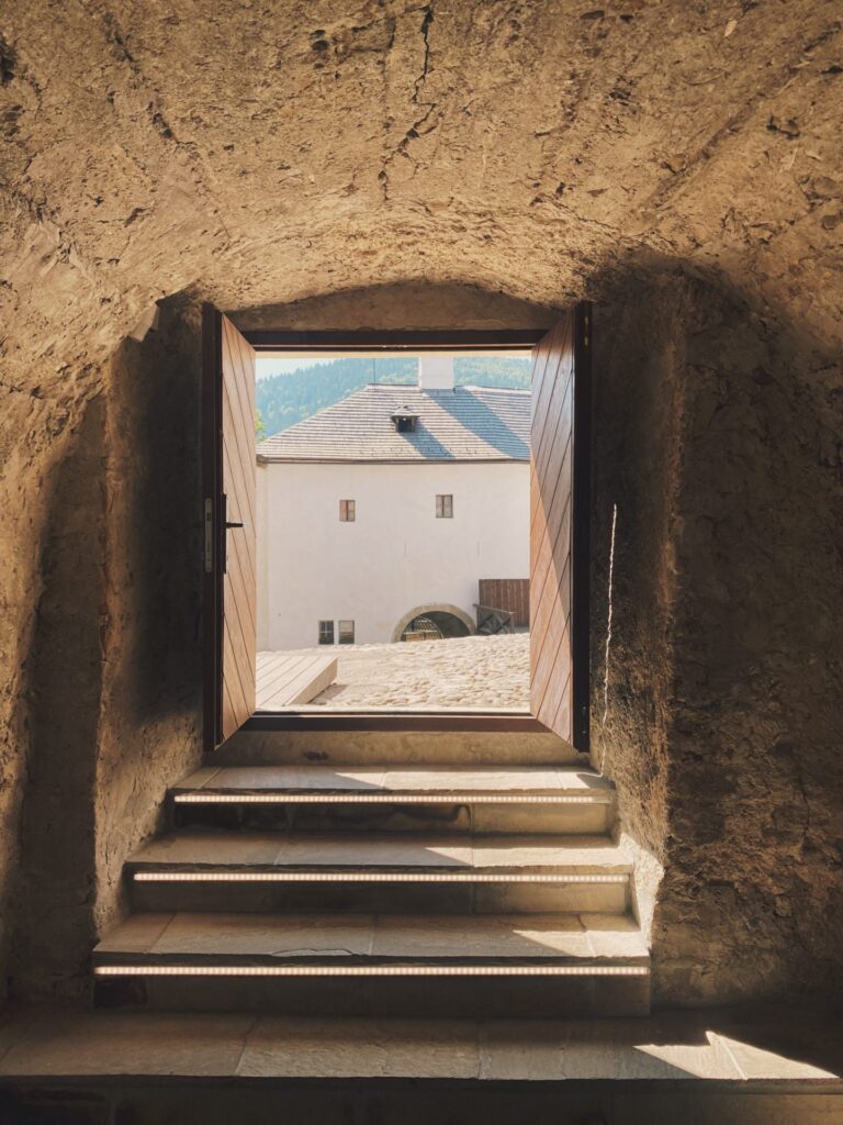 Open wooden doors at Orava Castle reveal a sunny courtyard and white building