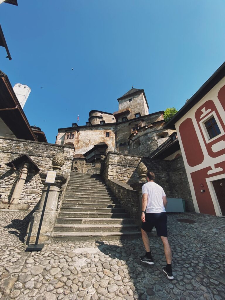 A man walks up stone stairs toward the towering Orava Castle