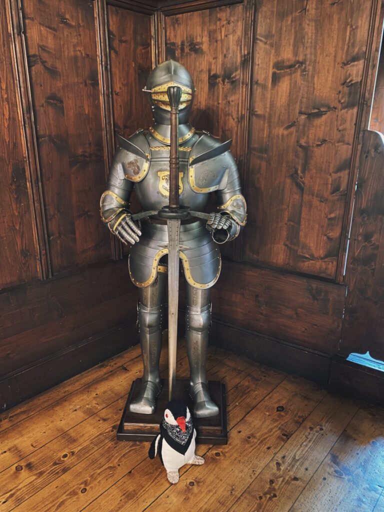 A suit of armor stands in Orava Castle with a plush penguin below
