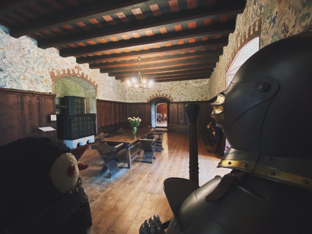 Plush penguin toy Miško looks at a suit of armor inside Orava Castle