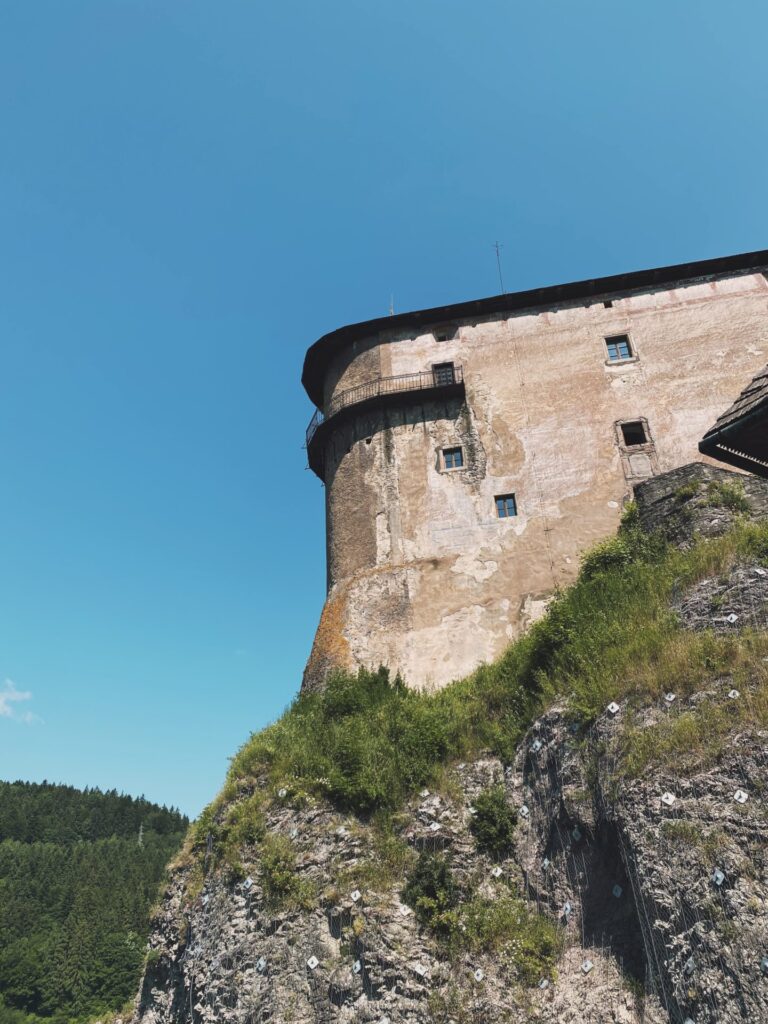 Orava Castle perched high on a steep rocky cliff under a clear blue sky
