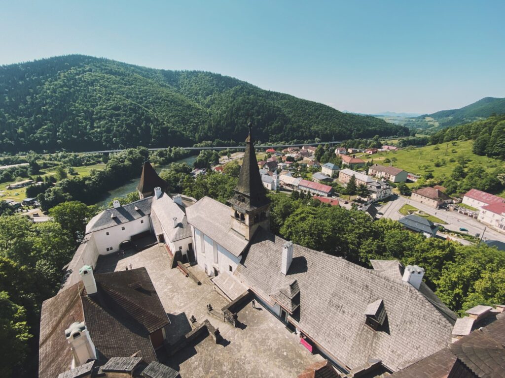 High angle view of Orava Castle overlooking a village and forested mountains
