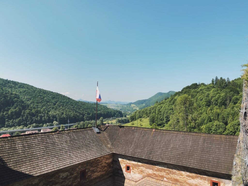 Slovak flag flying over the shingled roof of Orava Castle with green hills