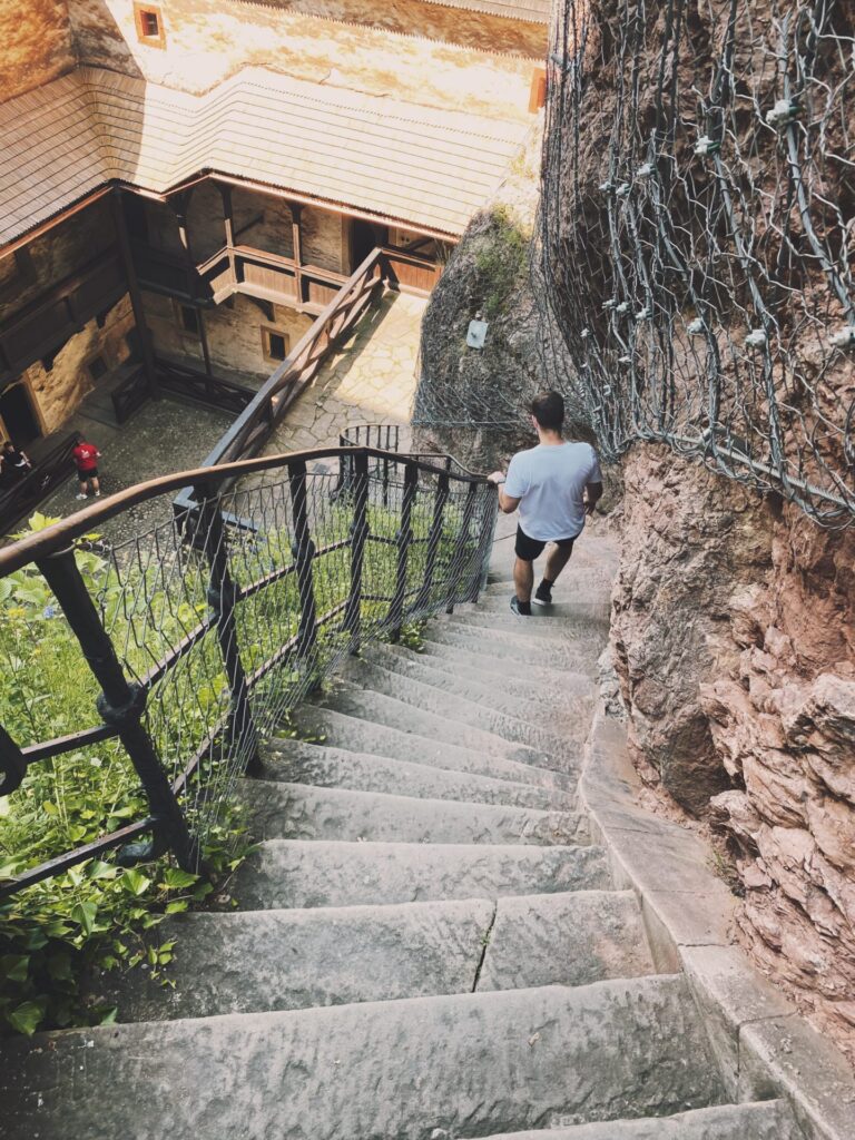 A man walks down stone stairs at Orava Castle beside a rock wall