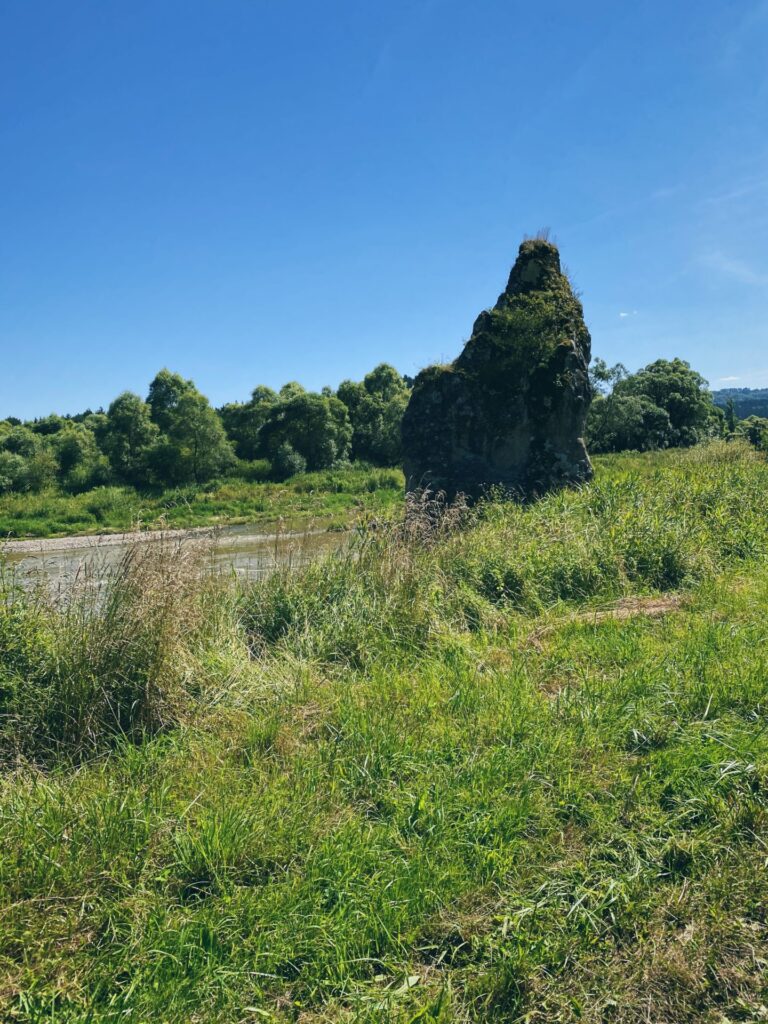Large rock formation rising above a grassy field near a river