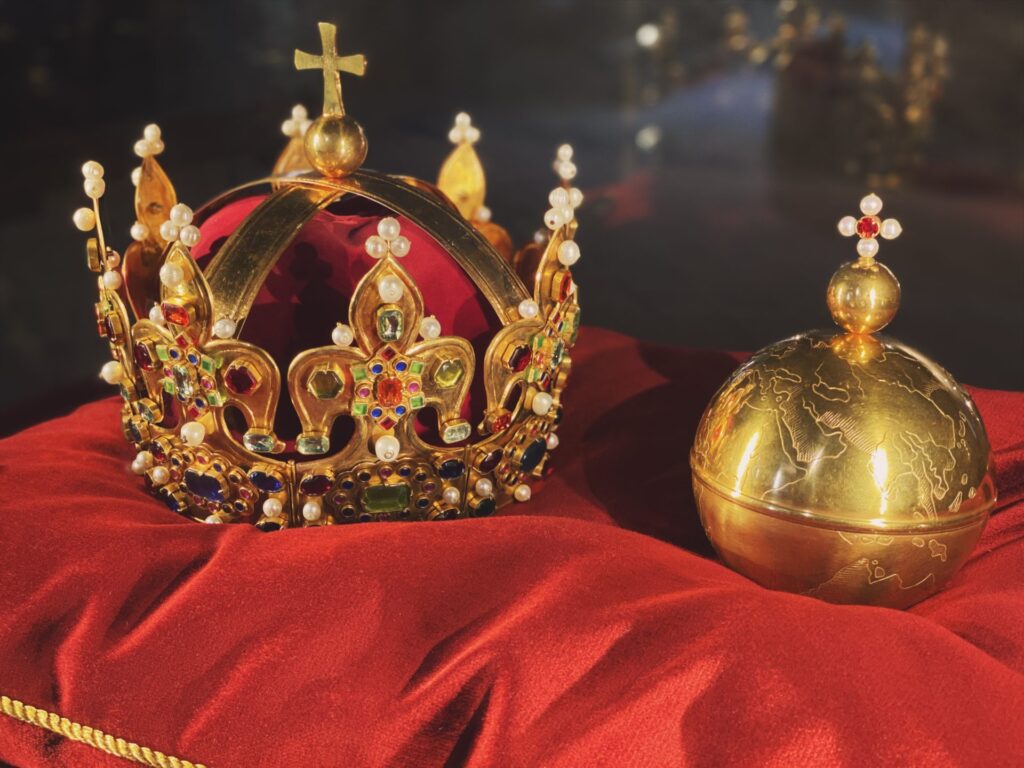 Ornate gold crown and royal orb resting on a red velvet cushion