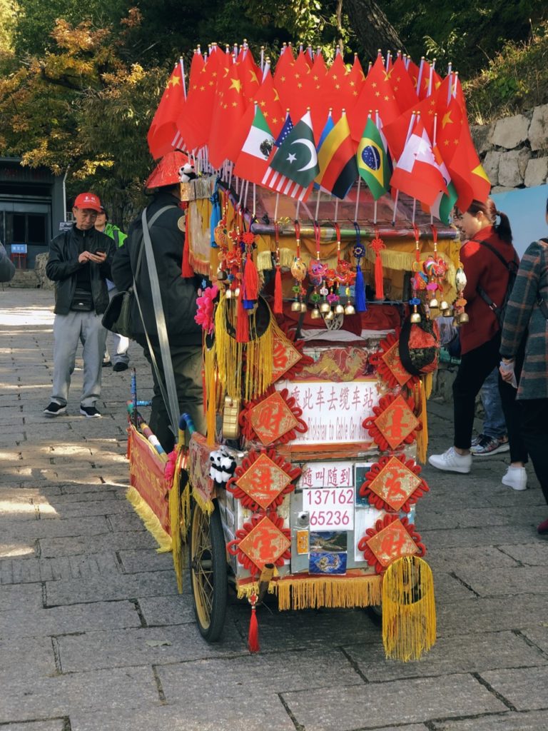 A decorated rickshaw adorned with many flags at the Great Wall of China