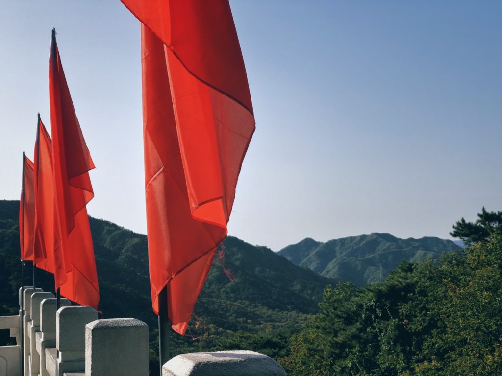 Bright red flags fly along the Great Wall of China against green mountains