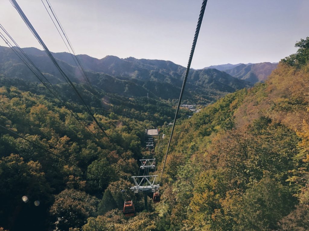 Cable cars descend over a forested valley toward the Great Wall of China