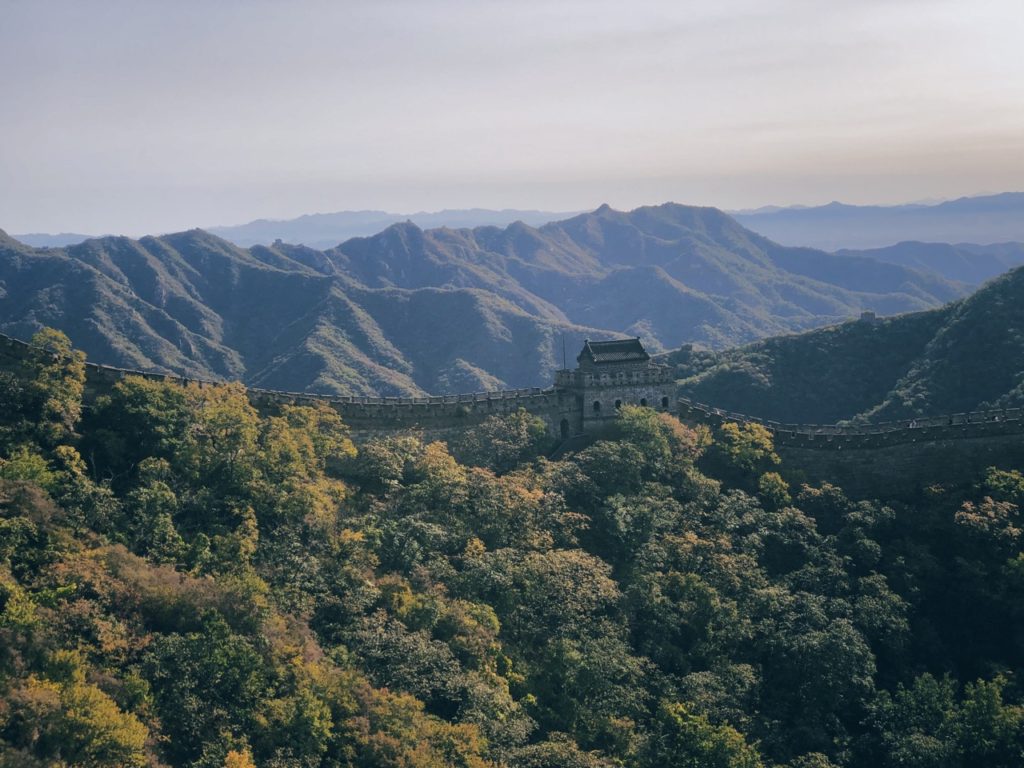 The Great Wall of China winds through lush green mountains at sunset