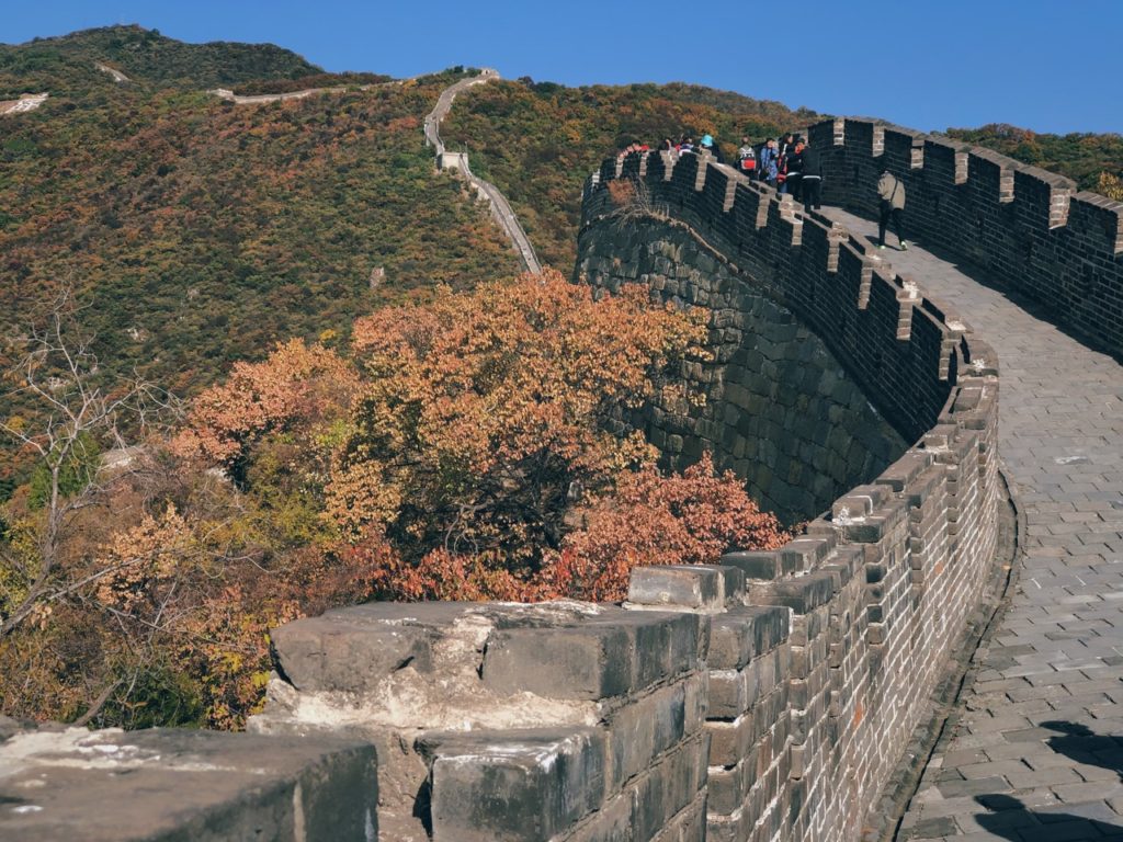Tourists walk along the Great Wall of China surrounded by autumn foliage