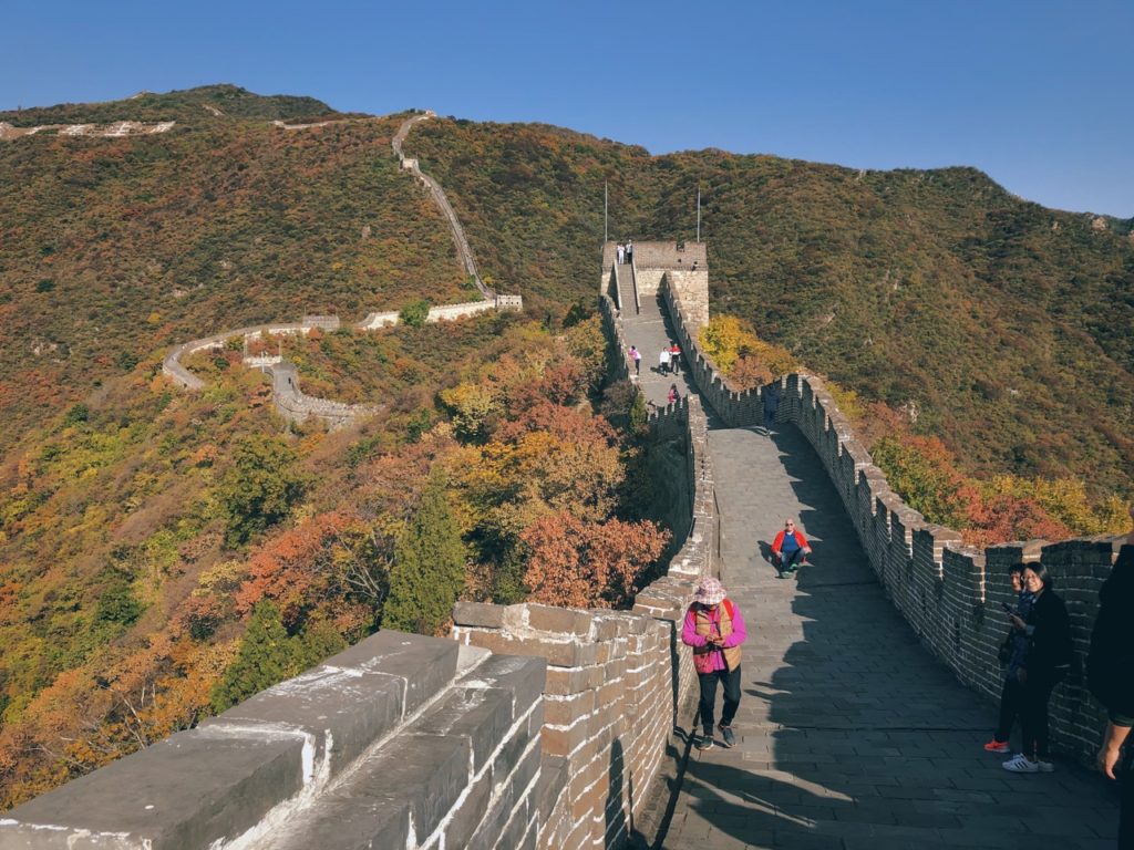 Tourists walk along the Great Wall of China surrounded by autumn foliage