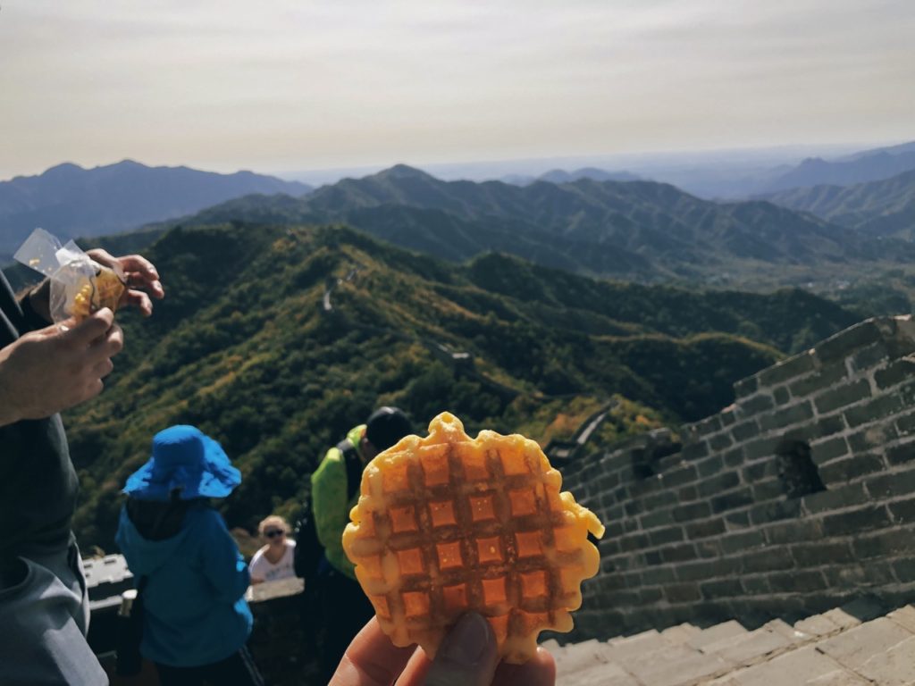 Hand holding a waffle with the Great Wall of China in the background
