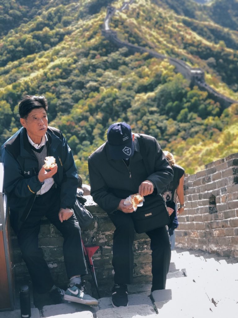 Two men eat snacks while sitting on the Great Wall of China