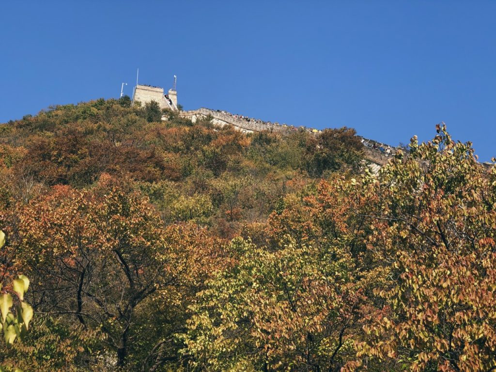 Tourists walk along the Great Wall of China surrounded by autumn foliage
