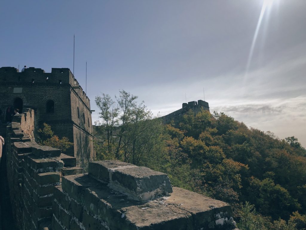 Sunlight shines over the Great Wall of China winding across a forested mountain