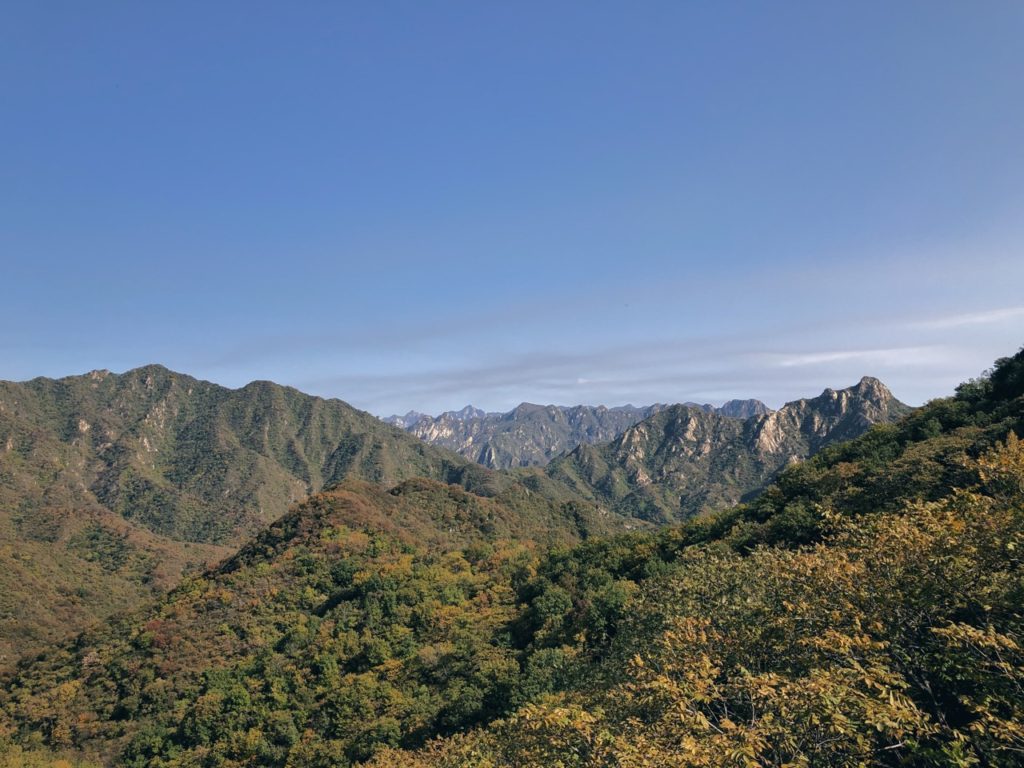 Lush green and autumn-colored mountains stretch toward a clear blue sky