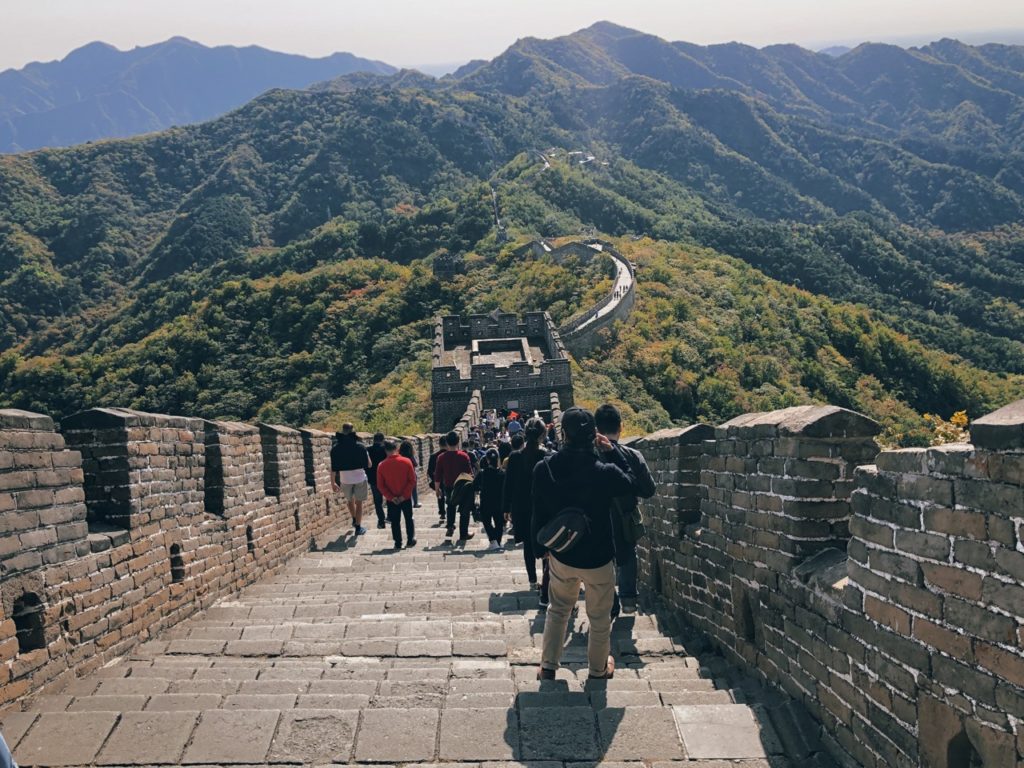Tourists walk along the Great Wall of China winding through lush green mountains