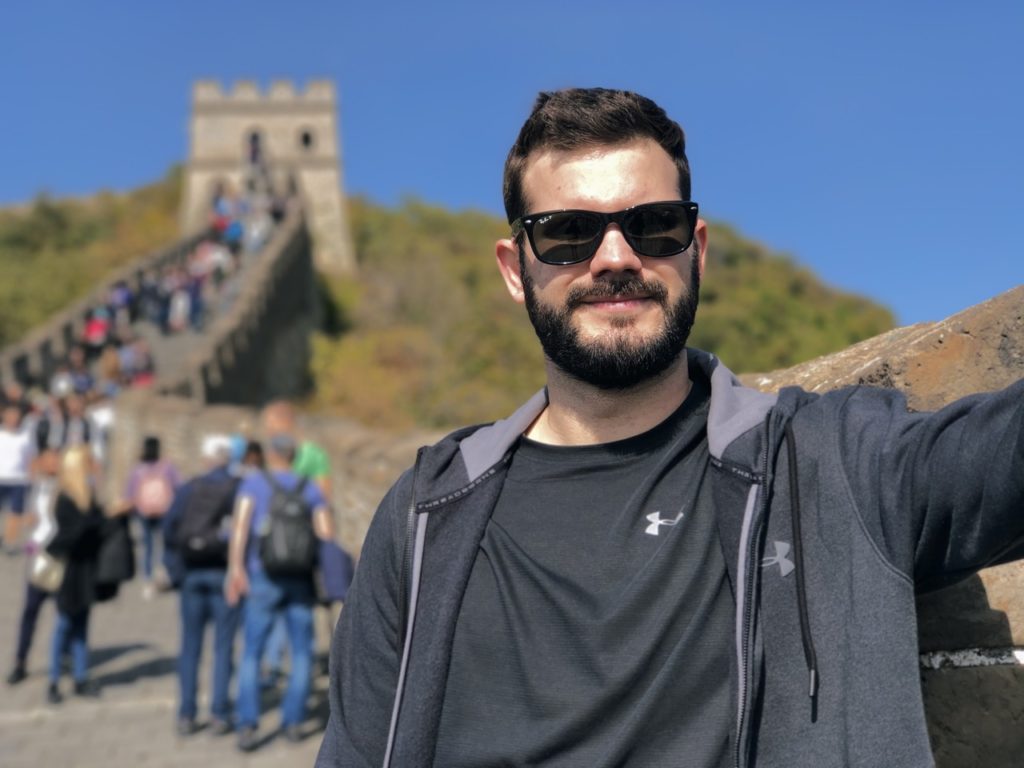 Man wearing sunglasses poses on the Great Wall of China with tourists behind
