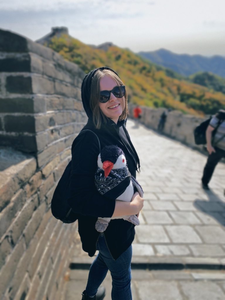 Woman in a hoodie holding a penguin plush on the Great Wall of China