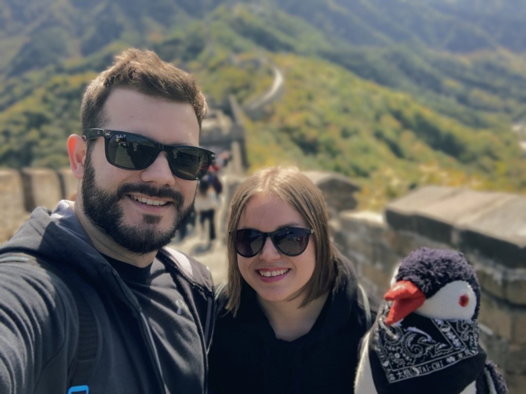 A couple and a penguin plushie pose on the Great Wall of China