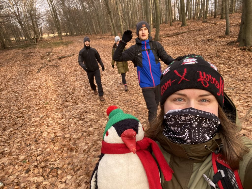 A woman takes a selfie with a penguin toy while friends walk behind