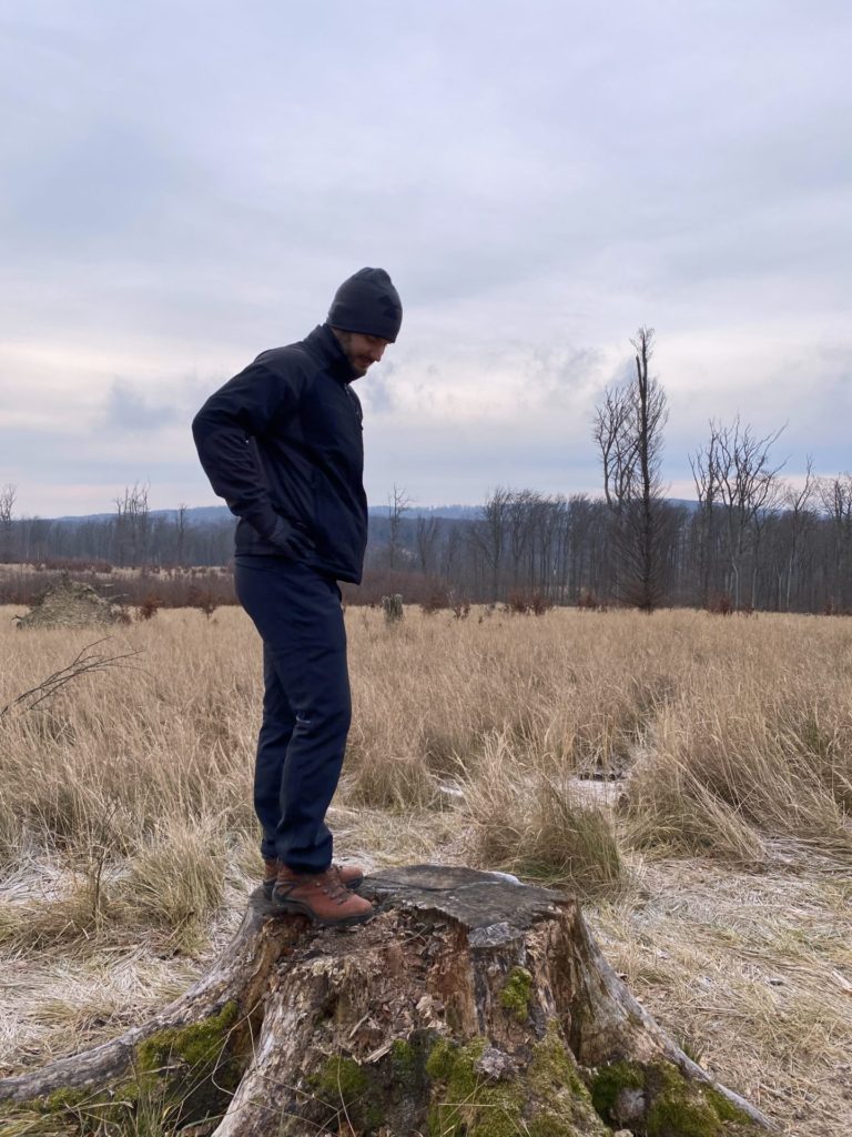 Man in a black jacket and beanie stands on a tree stump