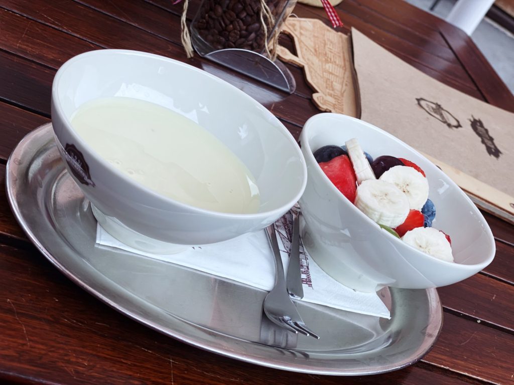 Two white bowls, one with yogurt and one with fruit, on a metal tray
