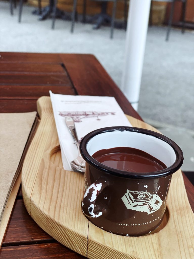 A brown enamel mug of hot chocolate sits on a wooden serving board