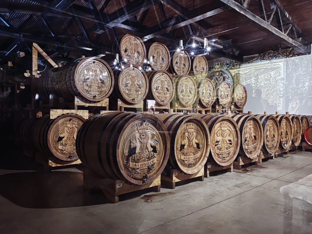 Rows of Nestville Whiskey barrels stacked in a dimly lit wooden cellar