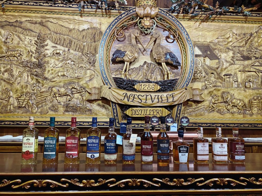 Bottles of Nestville whiskey lined up before an ornate wooden relief carving