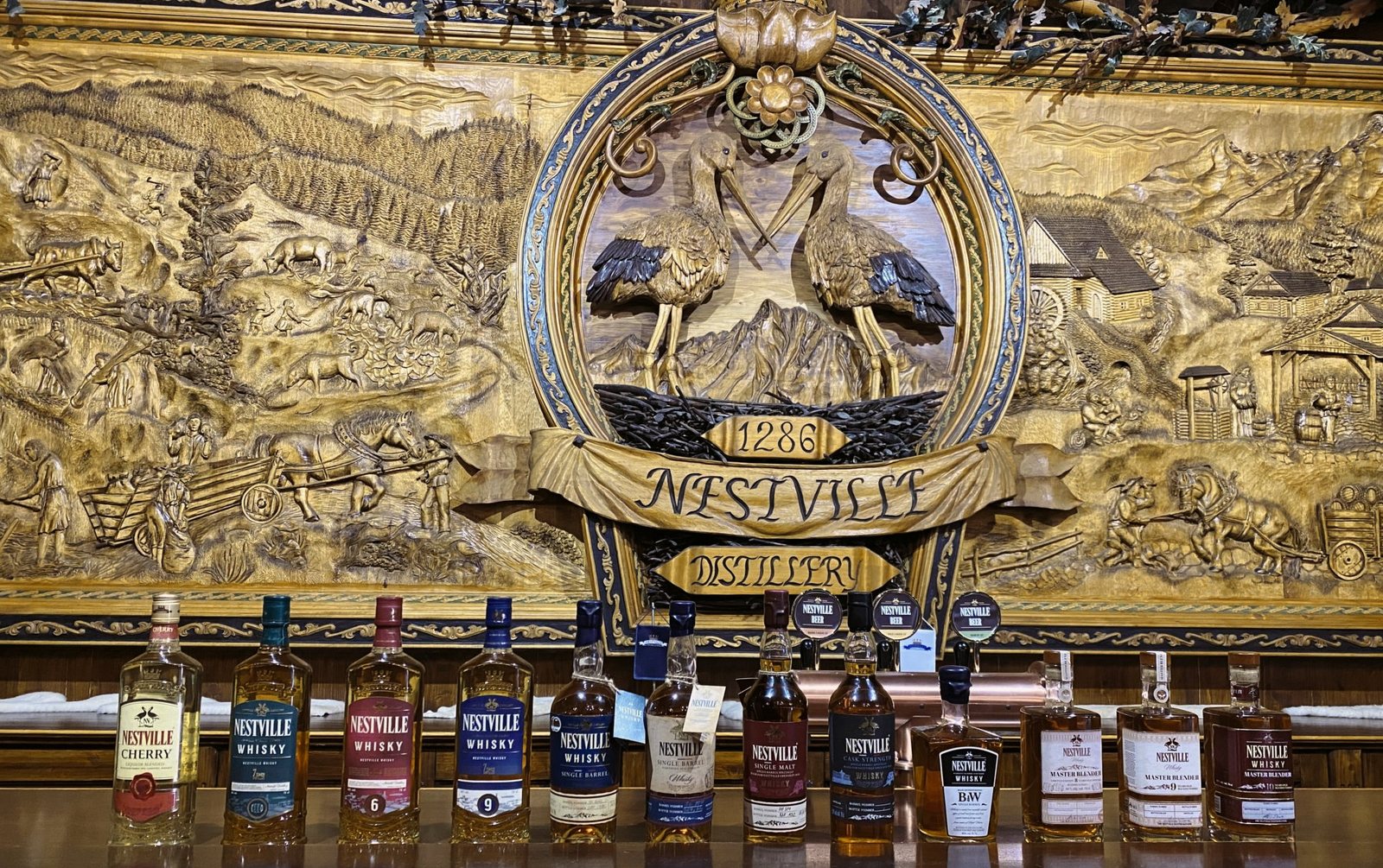 The carved gold Nestville Distillery emblem above a row of whiskey bottles, Slovakia