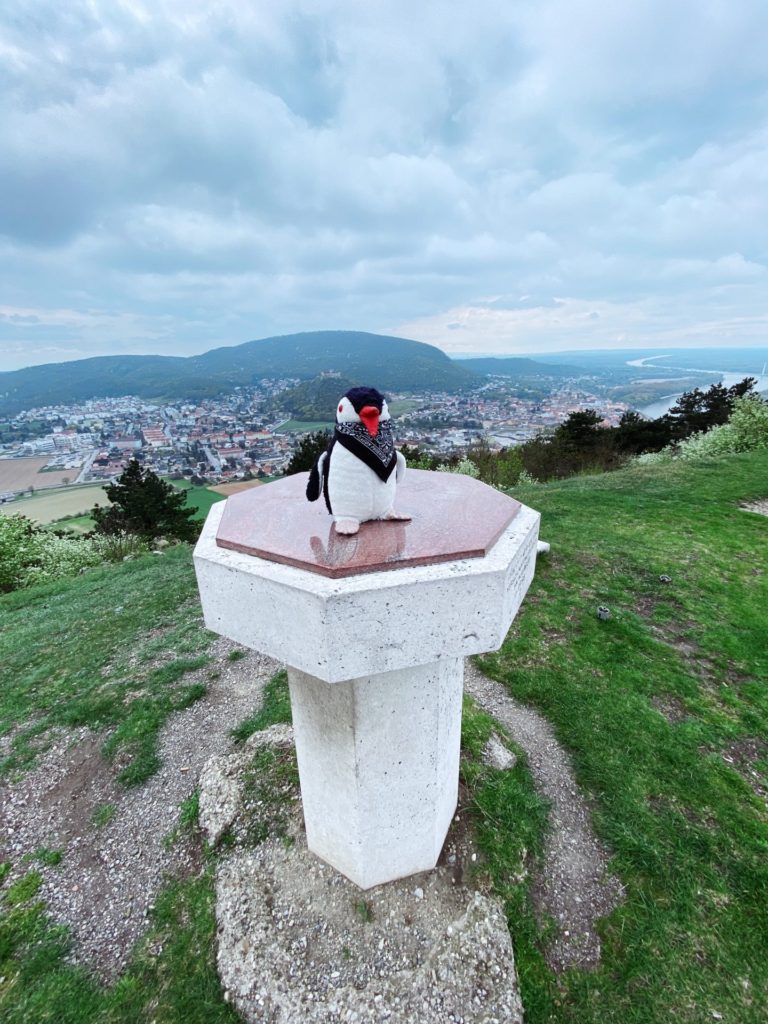 A plush penguin toy stands on a stone pedestal overlooking Braunsberg Hill Hainburg