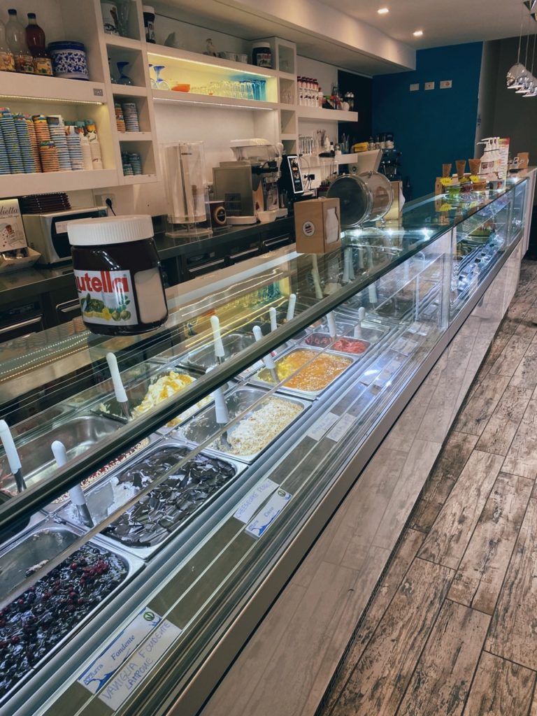 Glass display case filled with various flavors of gelato in an Alghero shop