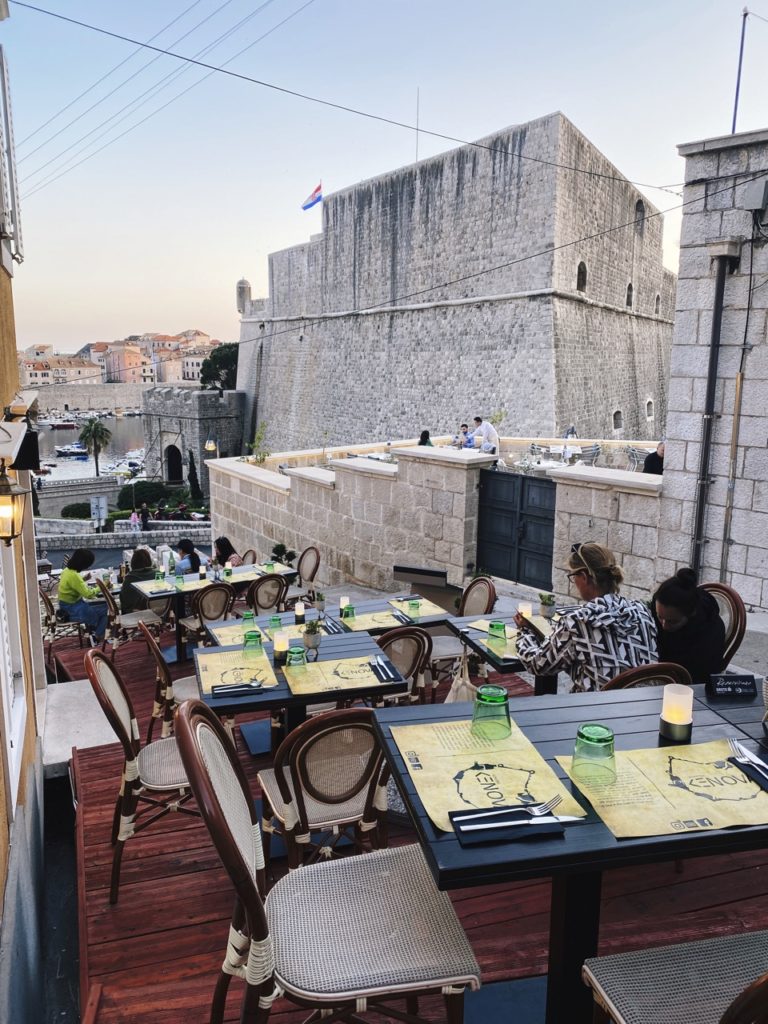Outdoor dining terrace in Dubrovnik overlooking a historic stone fortress and harbor