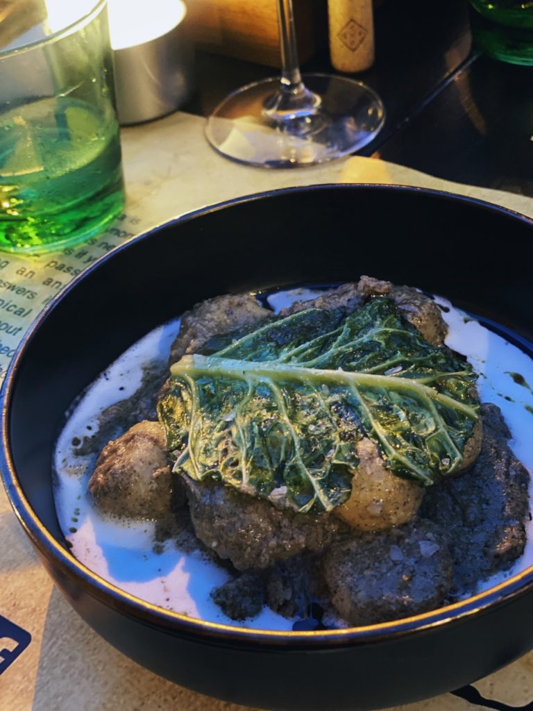 Gnocchi topped with a large green leaf in a dark bowl at dinner