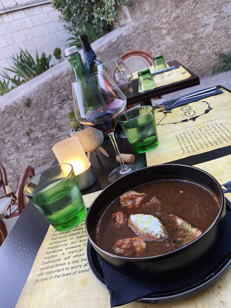 A bowl of dark soup, red wine, and water glasses on a table in Dubrovnik