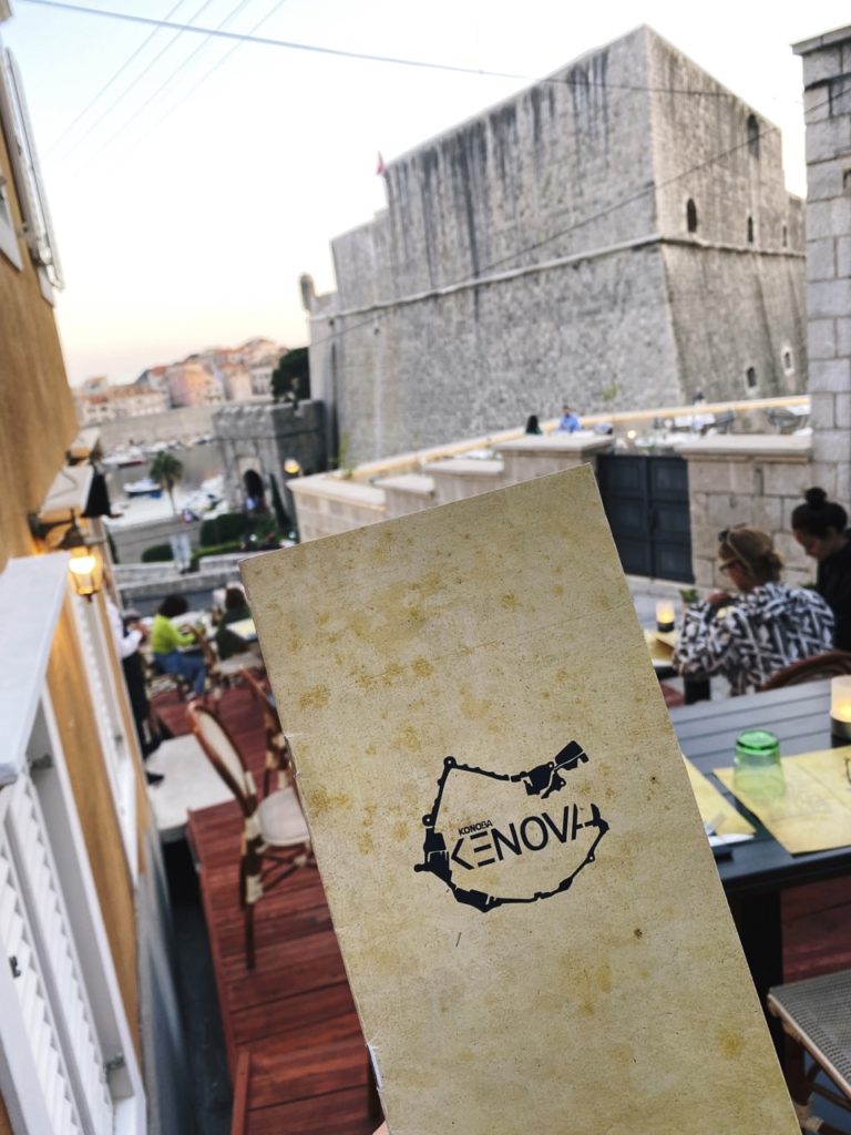 Menu held at a restaurant terrace overlooking the stone walls of Dubrovnik