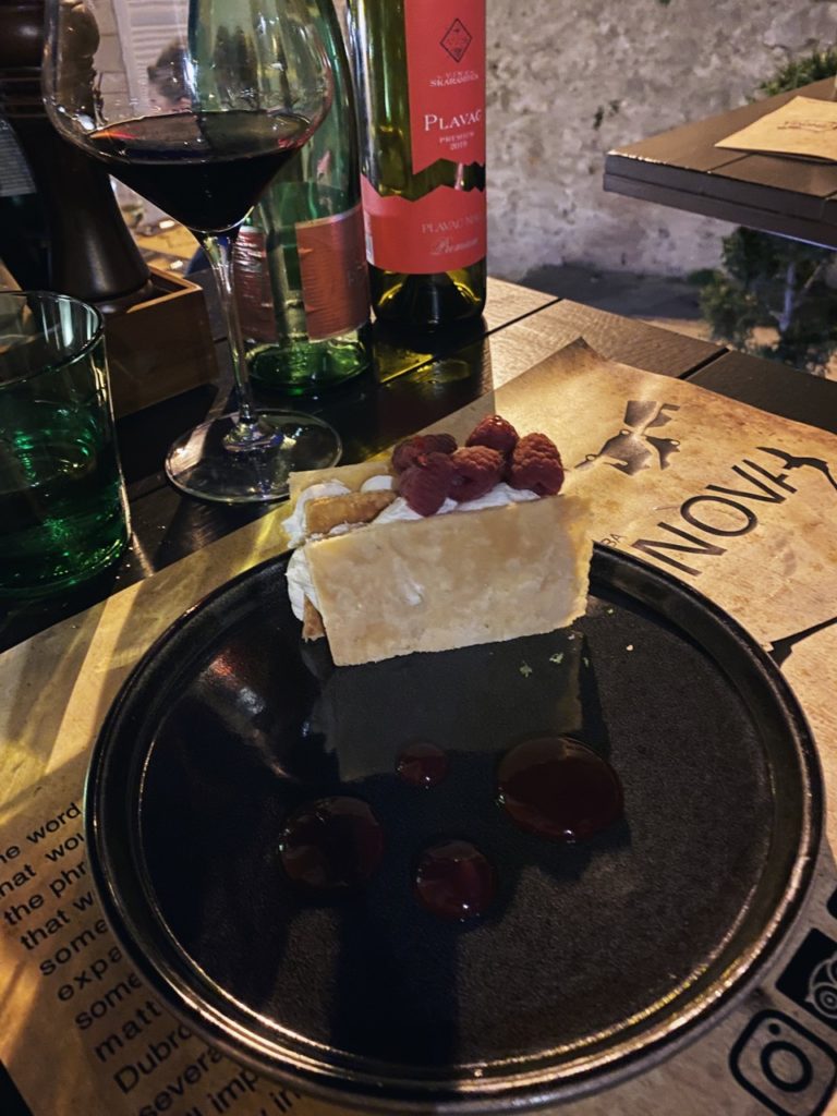 A layered pastry topped with raspberries sits on a plate with red sauce