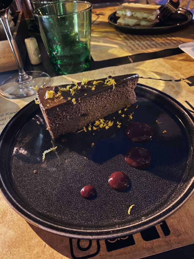 A slice of chocolate cake garnished with zest on a dark plate
