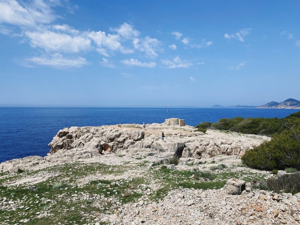 People walk on a rocky cliff overlooking the blue sea on Lokrum Island