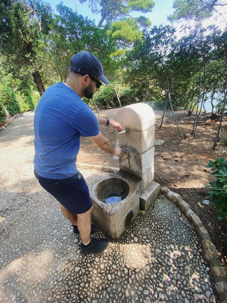 Man fills a water bottle at a stone fountain on Lokrum Island