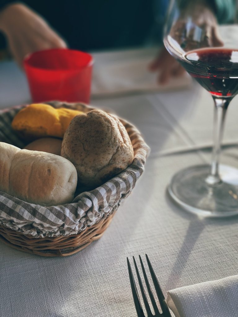 Basket of bread rolls next to a glass of red wine in Alghero